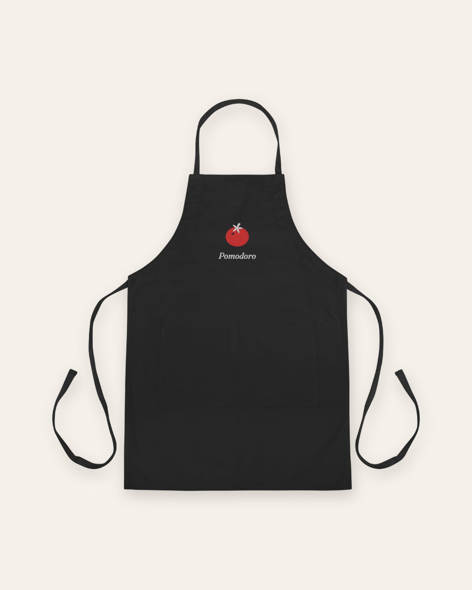 The Pomodoro Apron in Black, flat lay front, product shot on cream