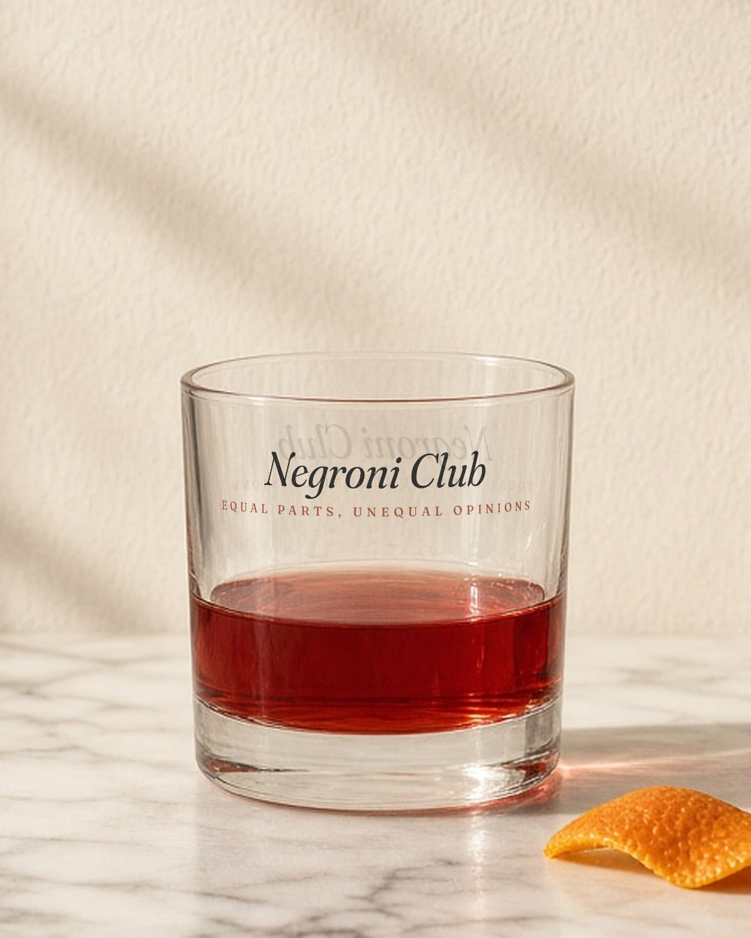The Negroni Club Rocks Glass in Clear 10.5 oz, Negroni on a marble counter with a twist of orange peel