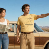 The Scenic Route Tee in Butter, couple beside a vintage wood-panel station wagon at a desert pull-off, she holds the map, he (Butter tee) points into the distance, hard sun