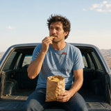 The Scenic Route Tee in Chambray, man in the Chambray tee on a station wagon tailgate eating gas-station snacks, desert view
