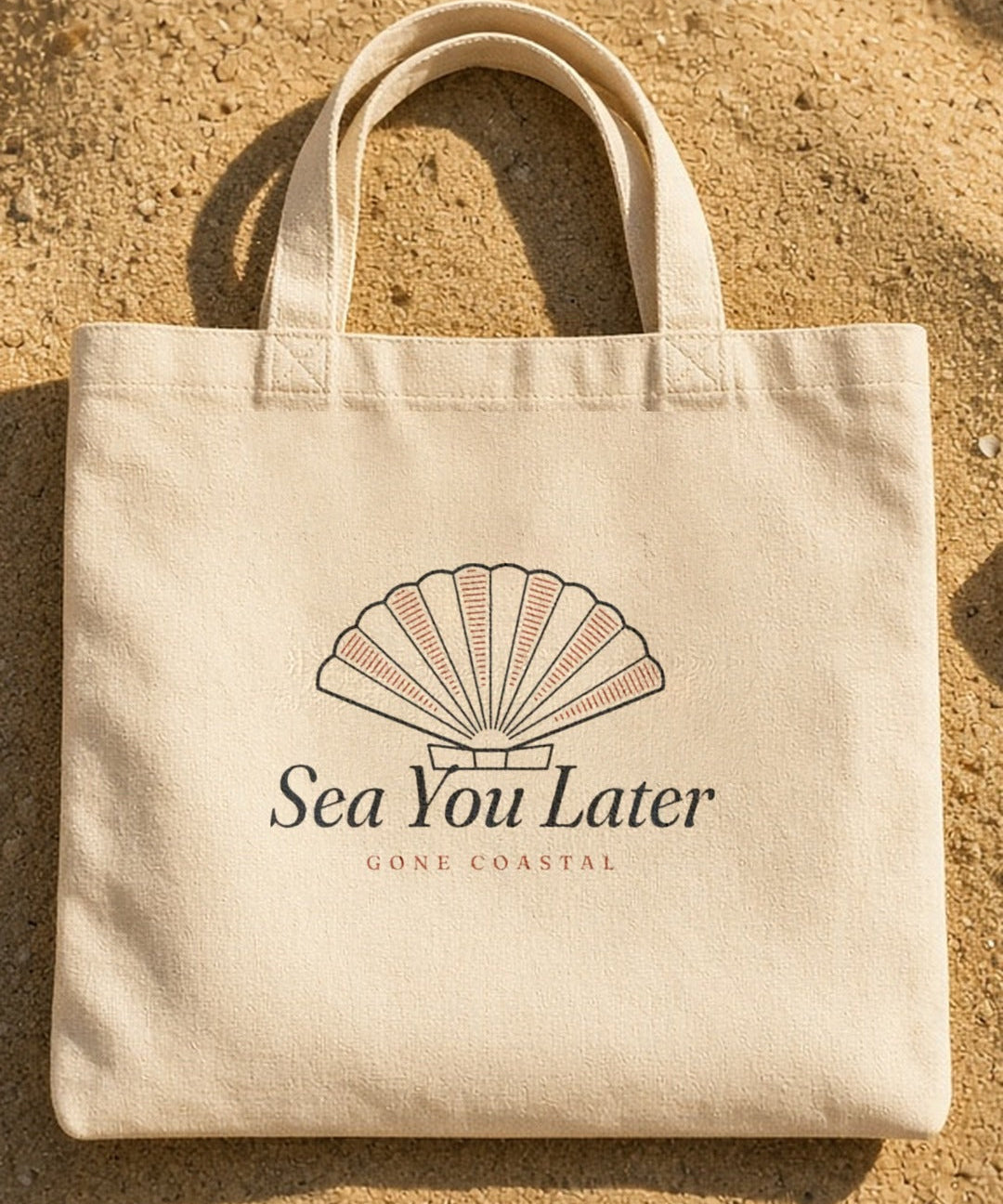 The Sea You Later Tote in Oyster, the tote on the sand with shells and a striped towel