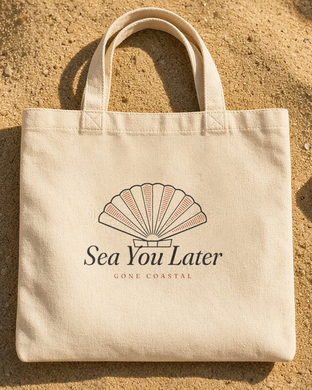 The Sea You Later Tote in Oyster, the tote on the sand with shells and a striped towel