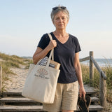 The Sea You Later Tote in Oyster, woman on wooden dune steps above the beach, tote on her shoulder, sandals in hand