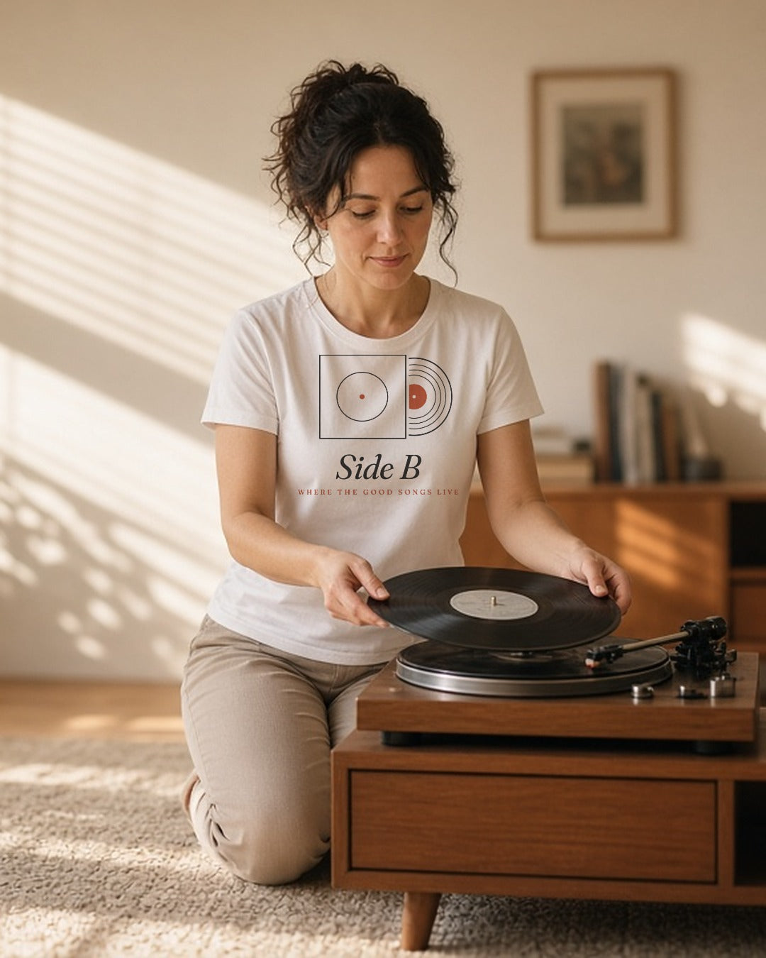 The Side B Tee in White, woman cross-legged on a rug flips a record on a turntable, sun streaks through the blinds