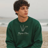 The Thyme Flies Crewneck in Forest Green, young man in a Forest Green crew sitting alone on a beach on an overcast day, looking off to the side