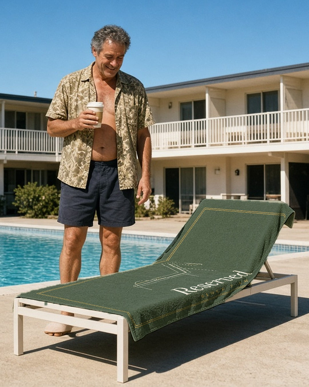 The Reserved Beach Towel in White, man (50s, open floral shirt, navy shorts, coffee cup) stands at the head of 'his' chaise beside a motel pool; the sage Reserved towel is laid lengthwise over the chaise, 'Reserved' facing camera; hard sun