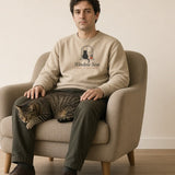 The Window Seat Crewneck in Sand, man in the Sand crew in a cream armchair, a tabby cat asleep on his lap, pale wall