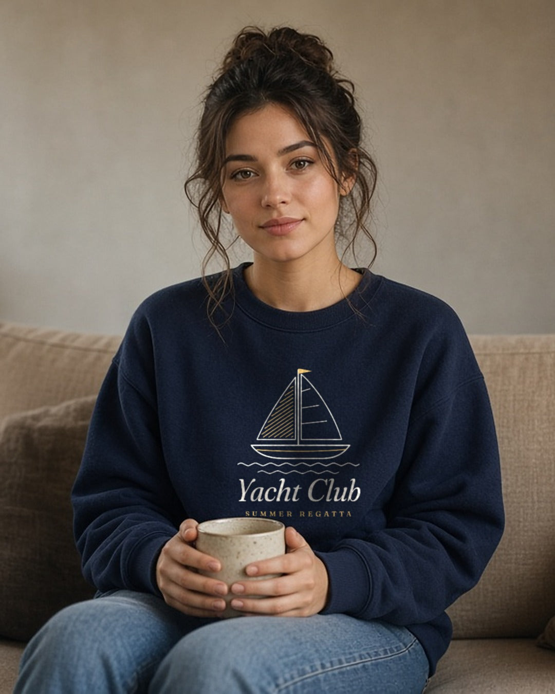 The Yacht Club Crewneck in Navy, woman on a linen sofa at home, mug held in her lap, window light